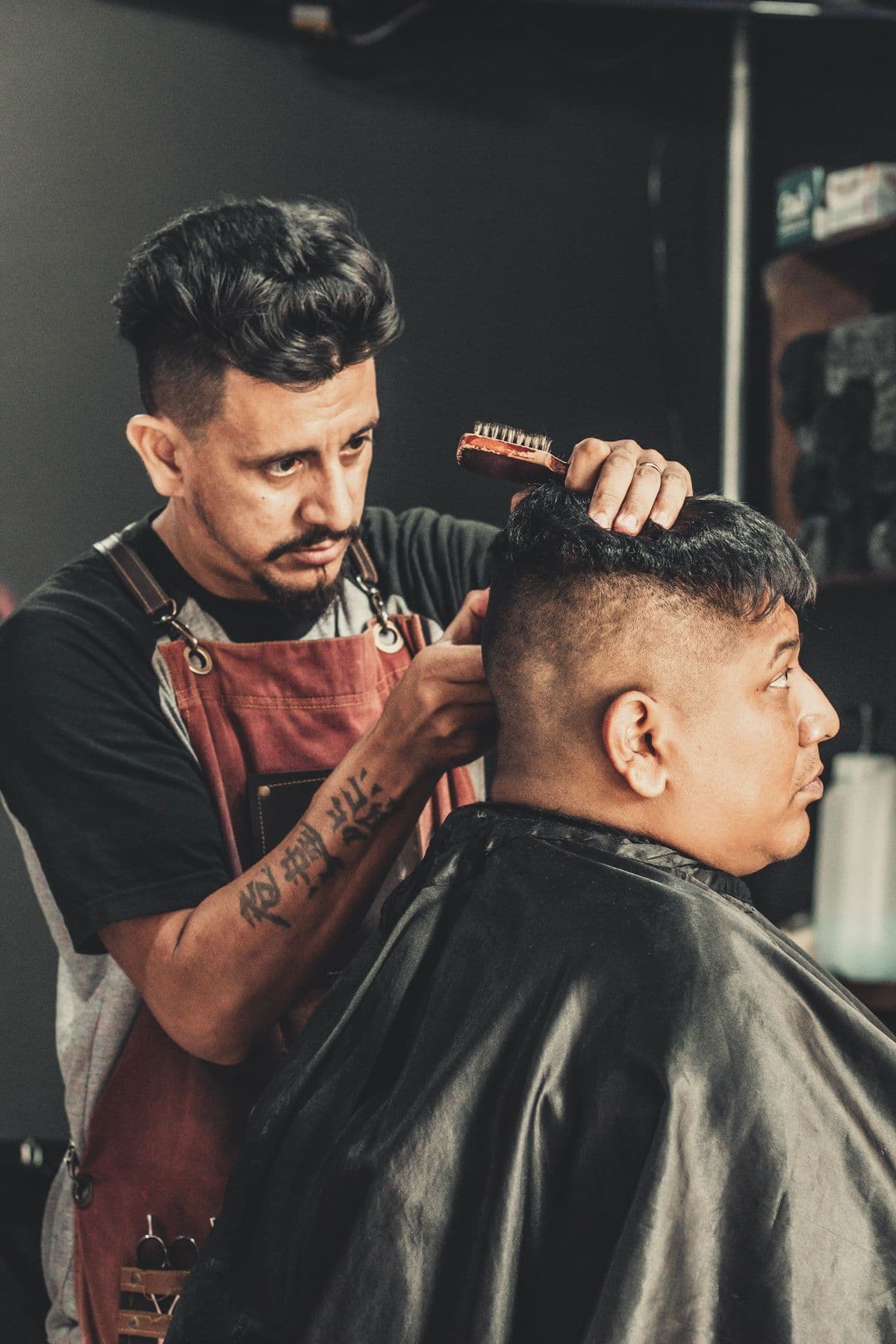 Un barbero con delantal de cuero peinando a su cliente antes del corte.